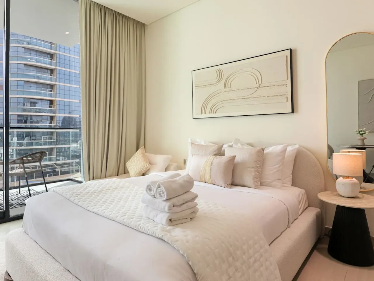 A bright bedroom with a neatly made bed and floor-to-ceiling windows.