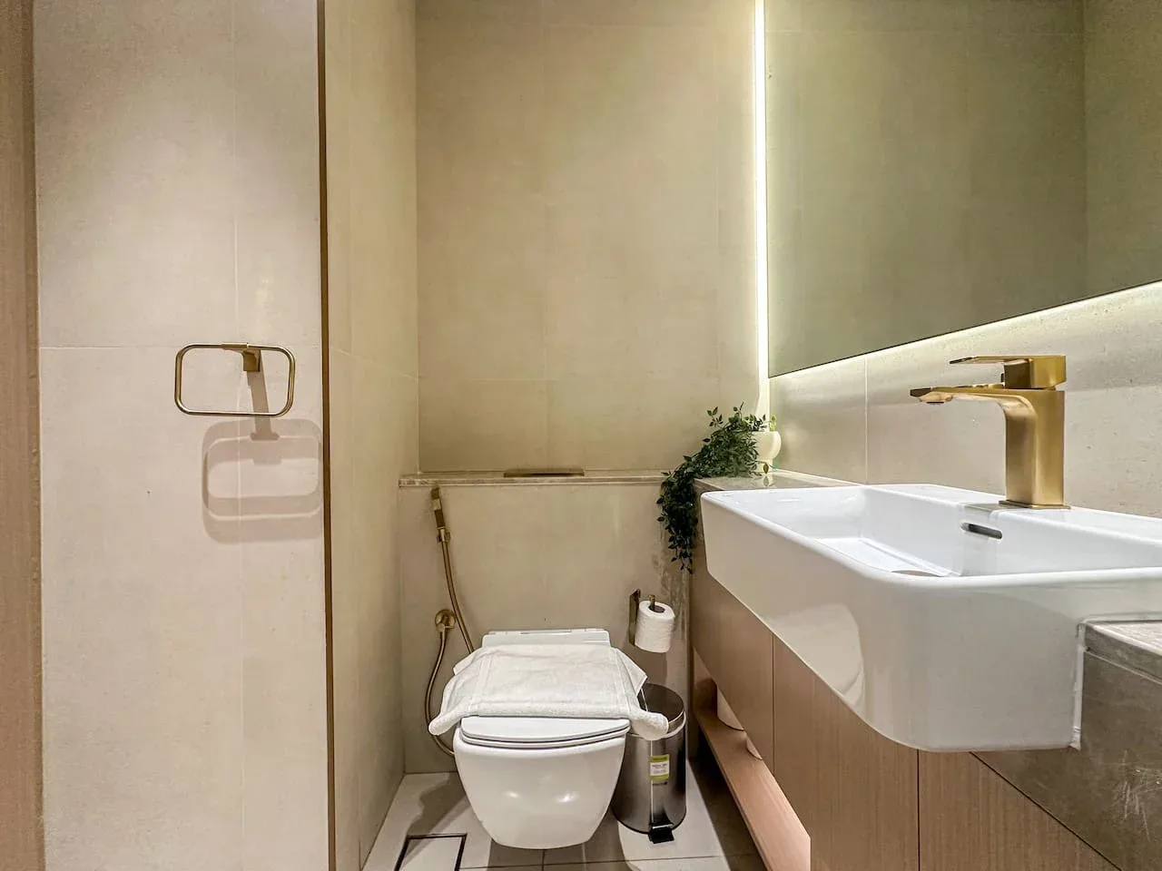A modern bathroom with a wall-mounted toilet, sink, and gold-colored faucet.
