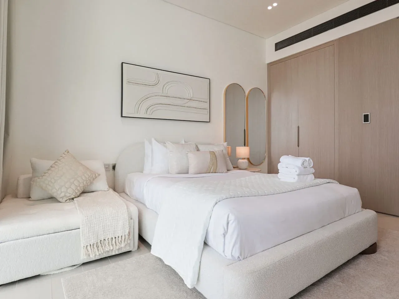 A bright bedroom with a neatly made bed and a cushioned seating area.