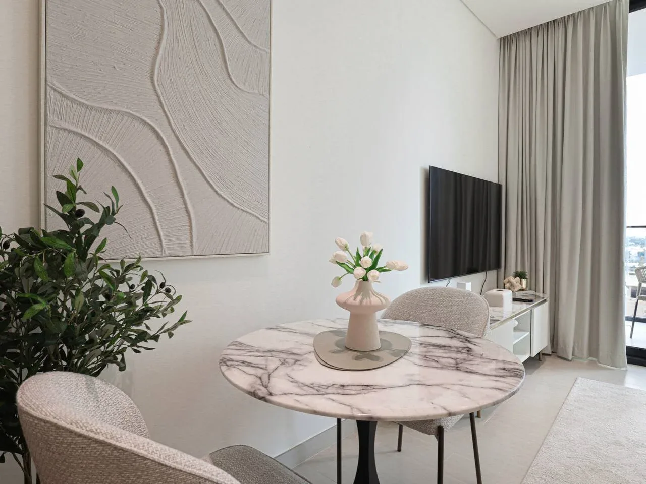 A bright sitting area with a round table, seating, and a wall-mounted television.