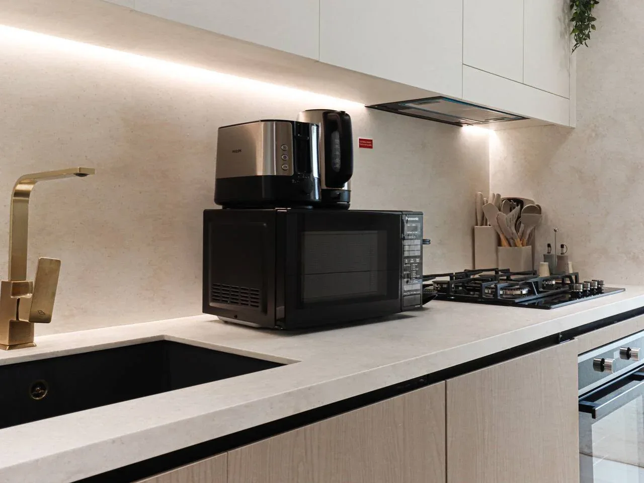 A modern kitchen counter with a microwave, kettle, and cooktop.