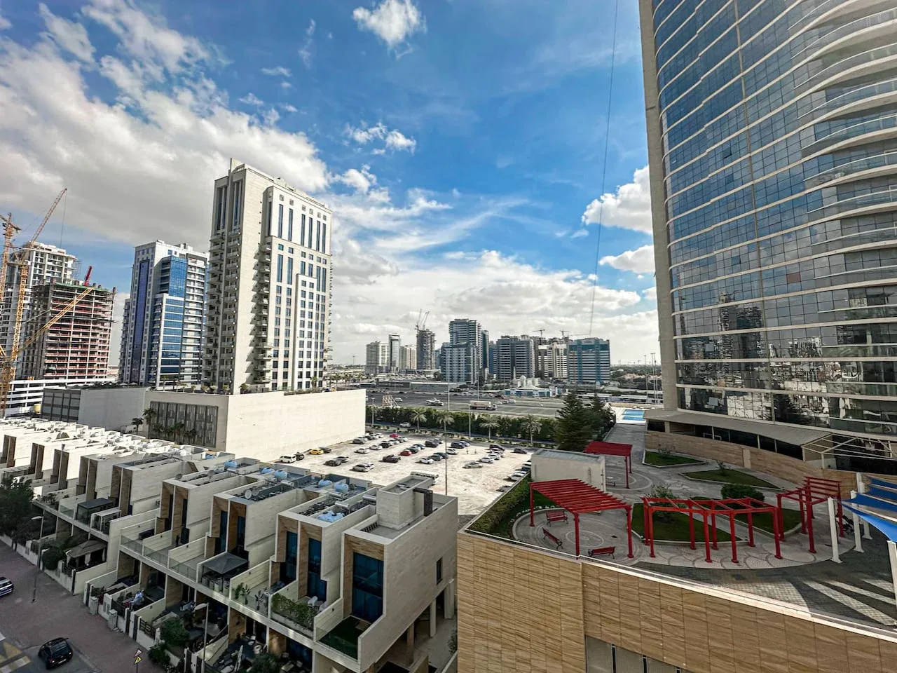 Cityscape with modern high-rise buildings and low-rise buildings under a partly cloudy sky.