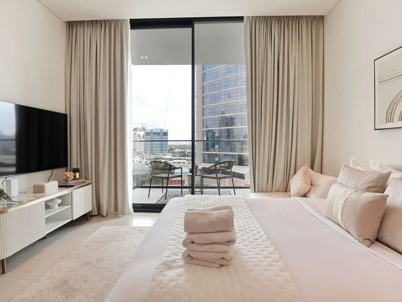 A bright bedroom with a large bed facing a floor-to-ceiling window and balcony.