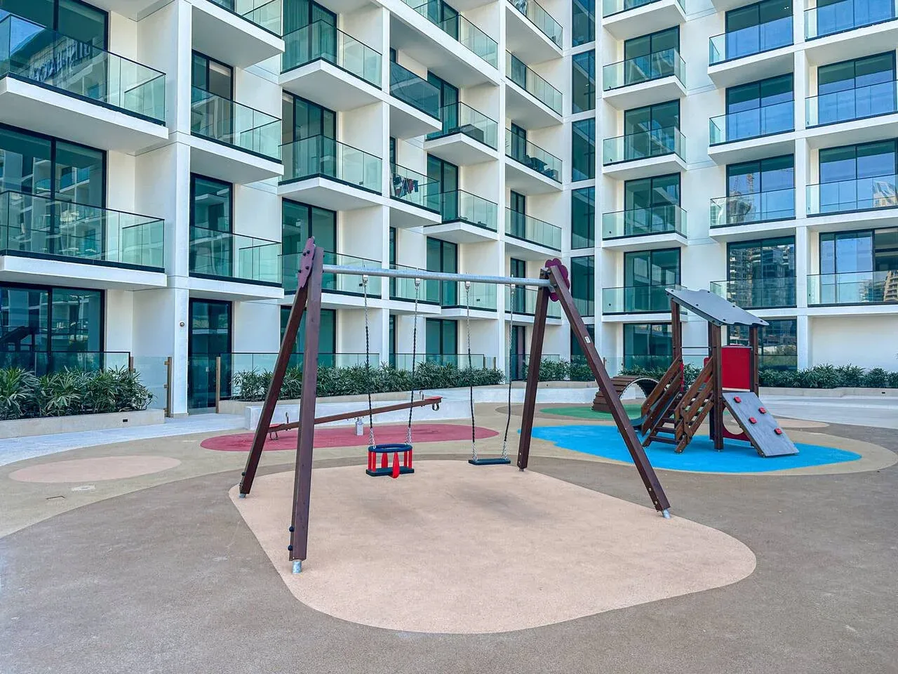 An outdoor playground with swings and a slide sits beside a modern apartment building.