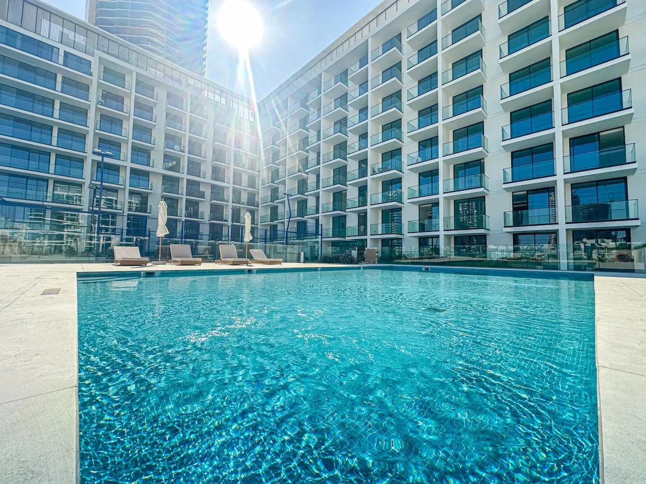 An outdoor swimming pool sits between modern multi-story buildings.