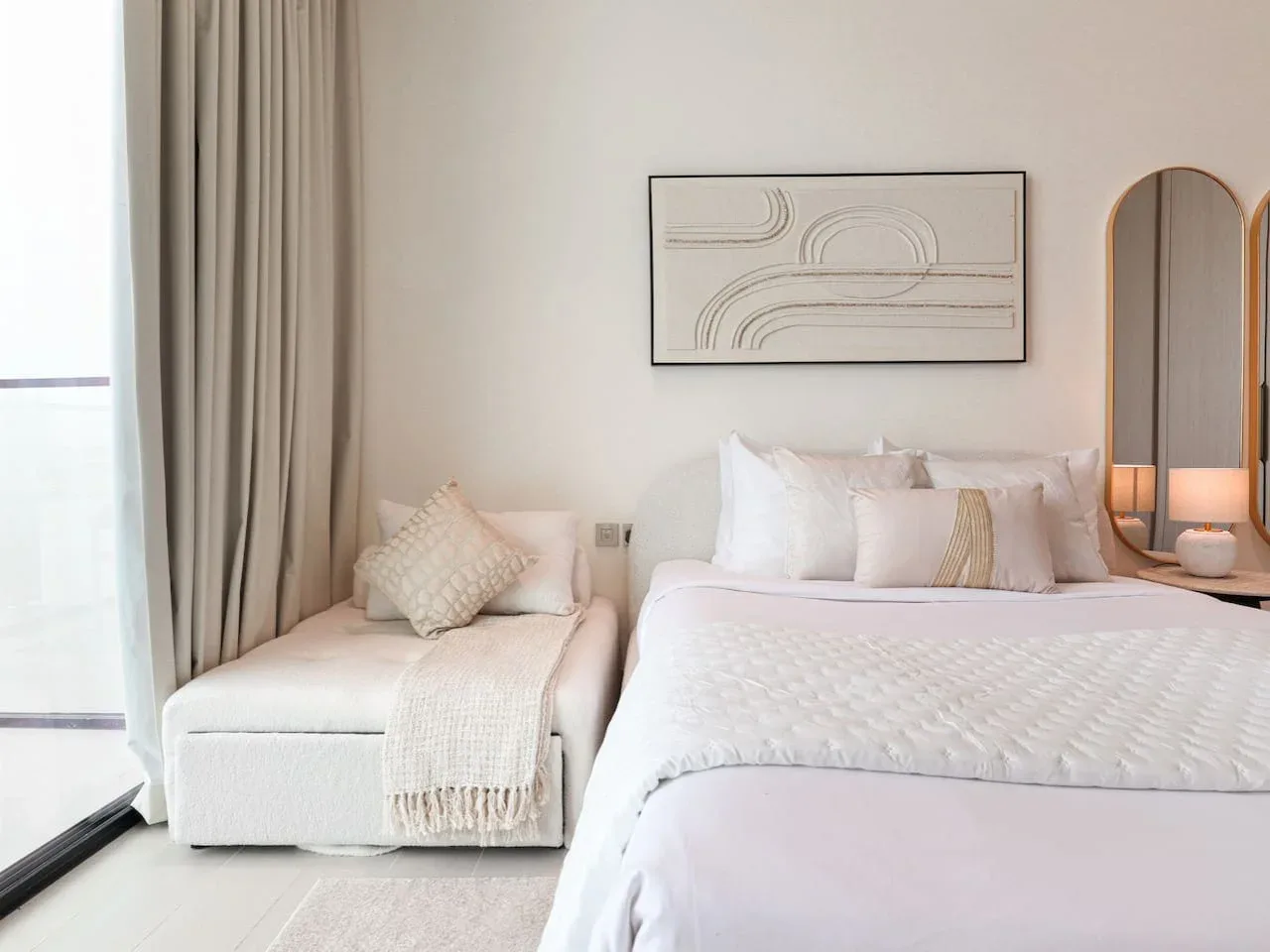 A bright bedroom with a large bed, a cushioned seat, and neutral decor.