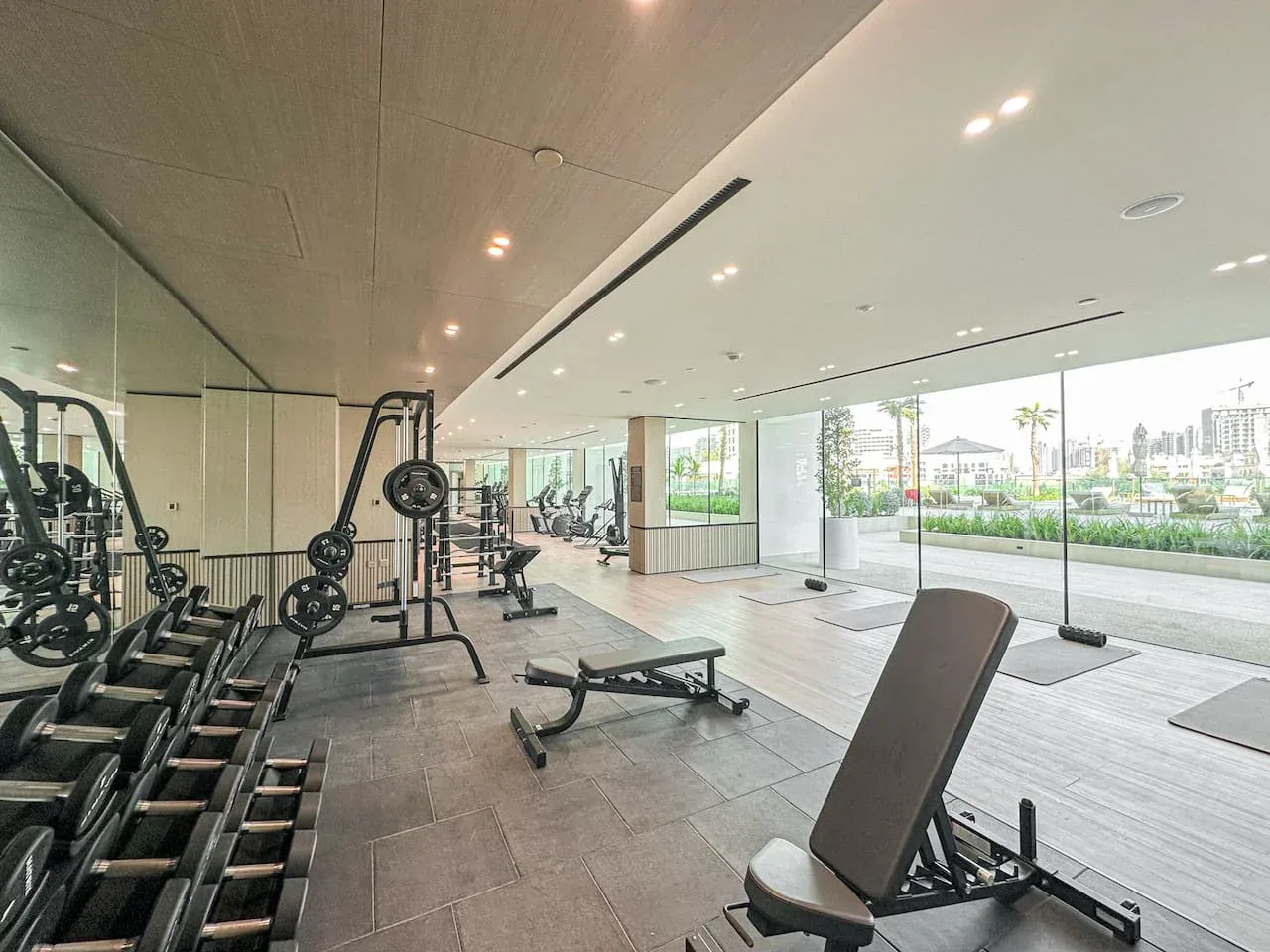 A bright gym with exercise equipment and large windows overlooking greenery.