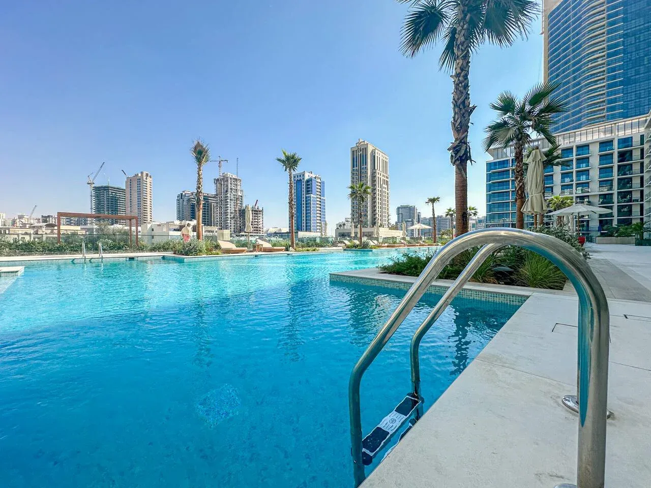 A swimming pool beside palm trees and modern high-rise buildings.