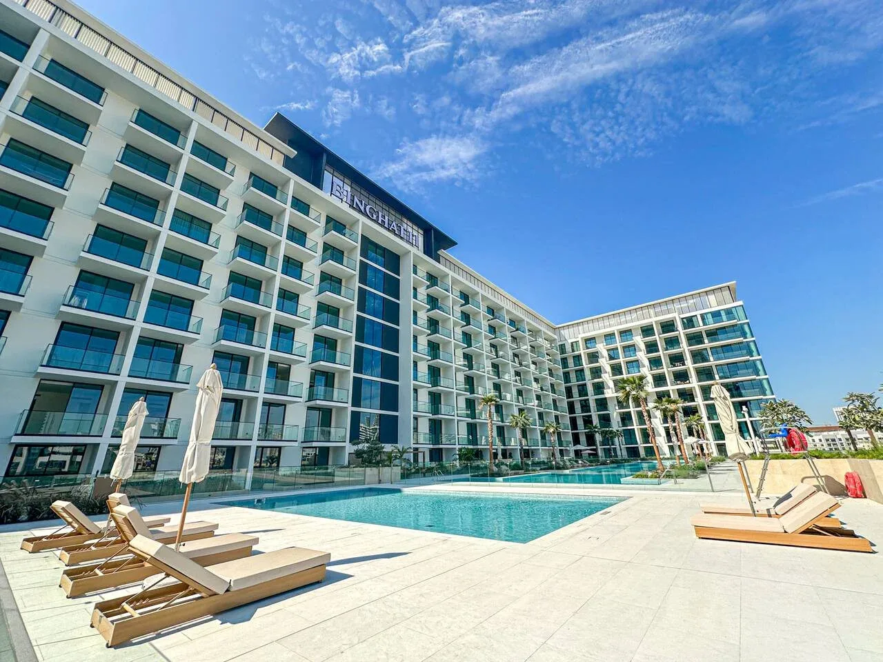 A swimming pool and loungers sit beside a large modern hotel building.