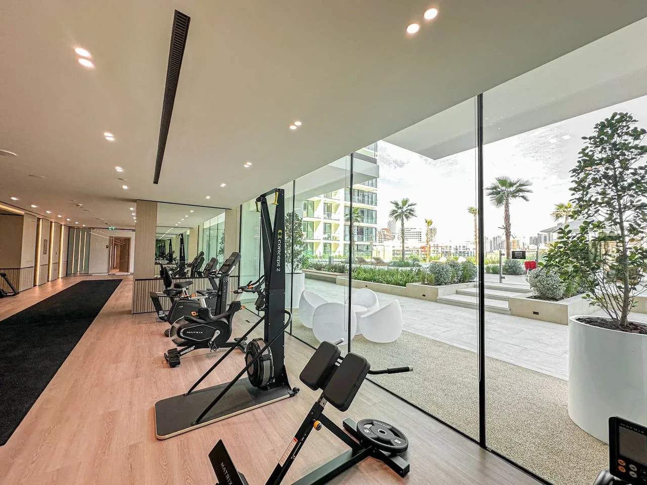 A gym with exercise equipment beside large windows overlooking an outdoor terrace.