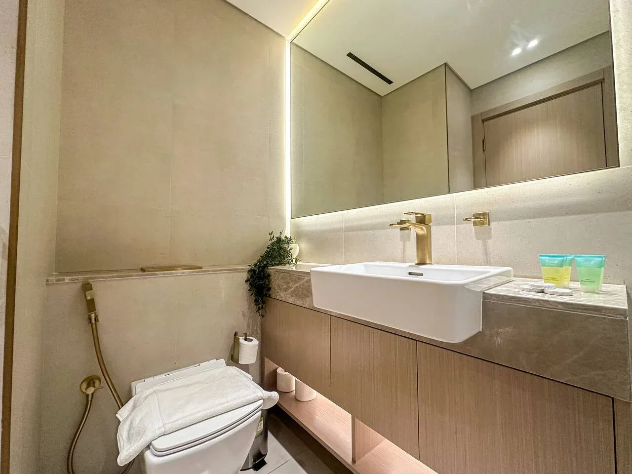 A modern bathroom with a wall-mounted sink, toilet, and large mirror.
