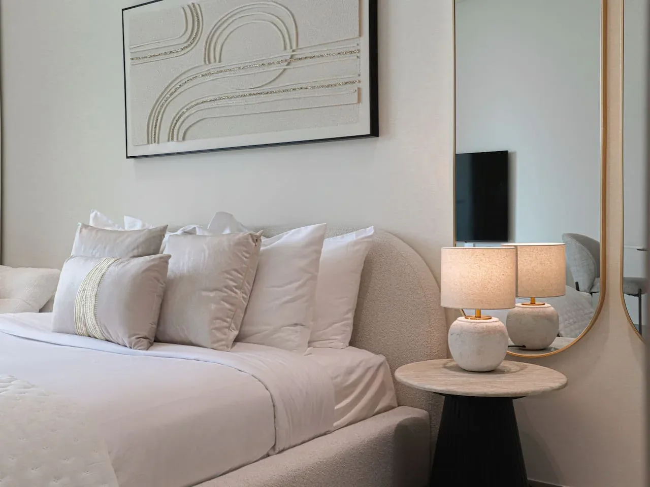 A neatly made bed sits beside a round table with two lit lamps.