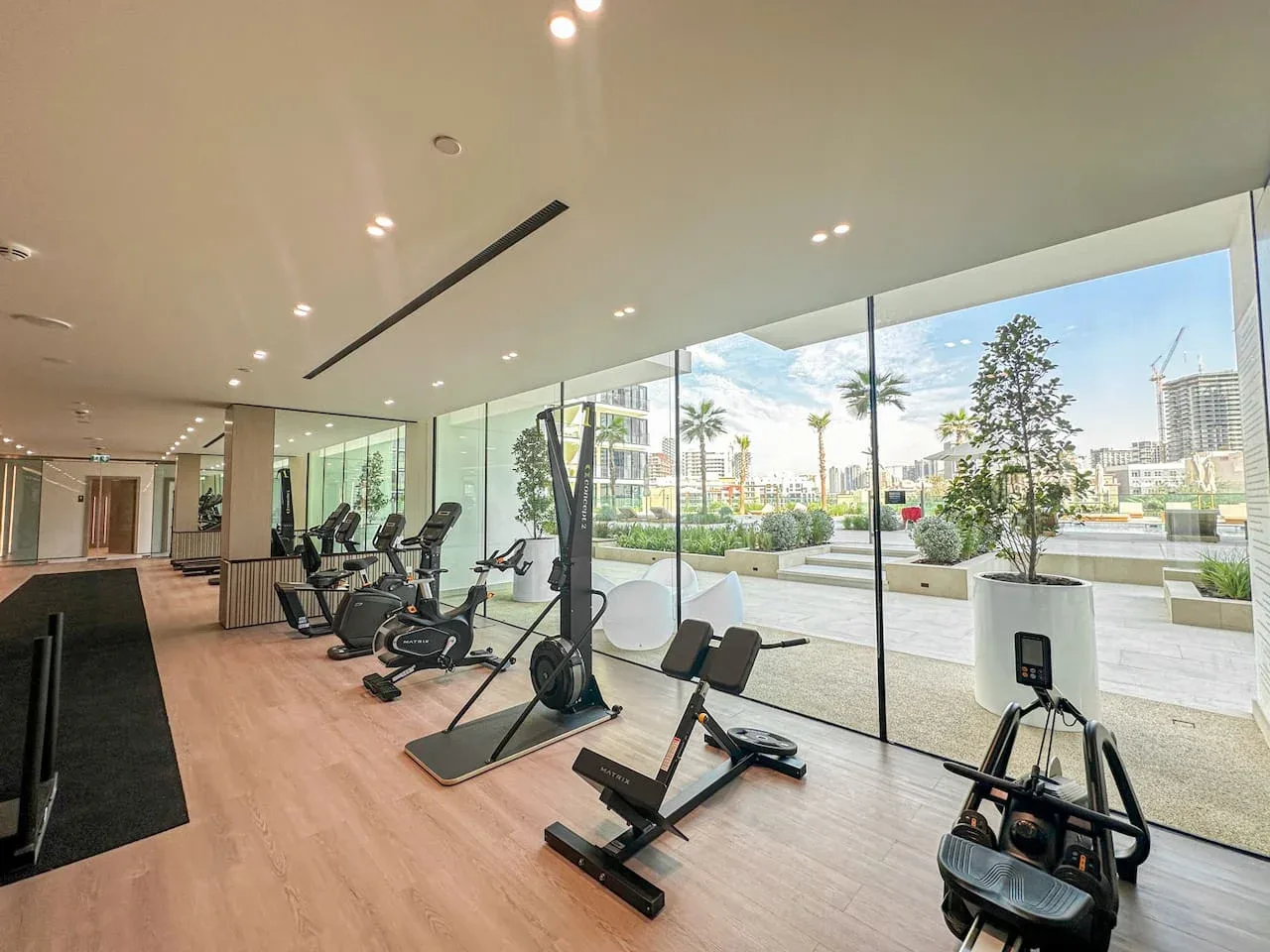 A gym with exercise machines beside floor-to-ceiling windows overlooking a landscaped outdoor area.