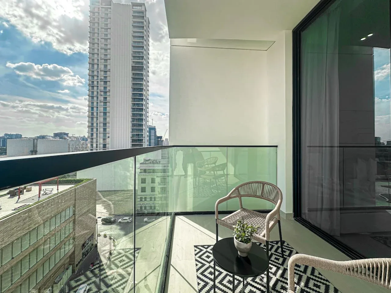 A balcony with seating and a glass railing overlooks nearby buildings.