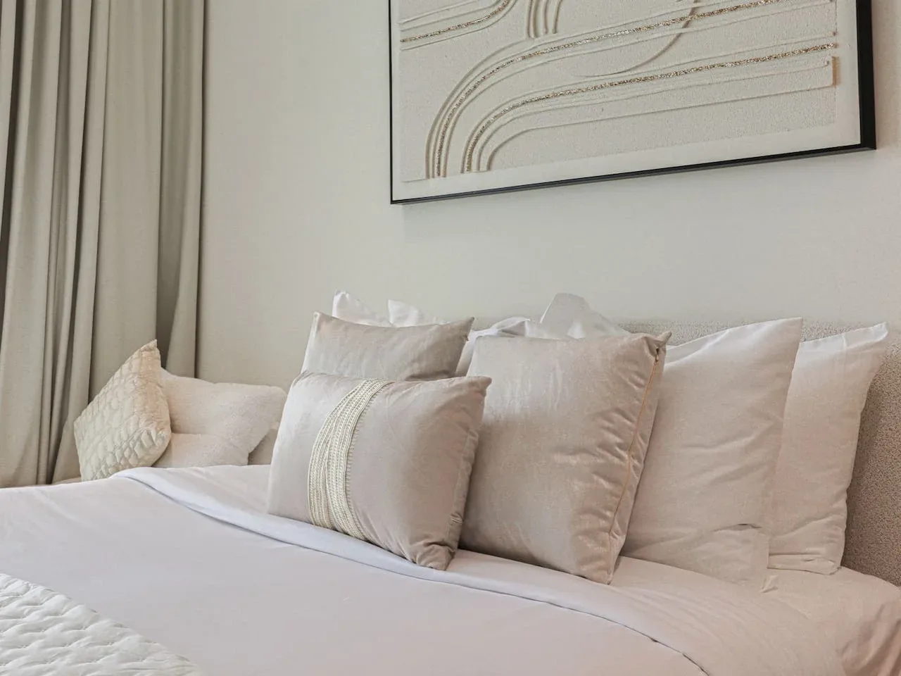 A neatly made bed with layered pillows sits beneath framed abstract artwork.
