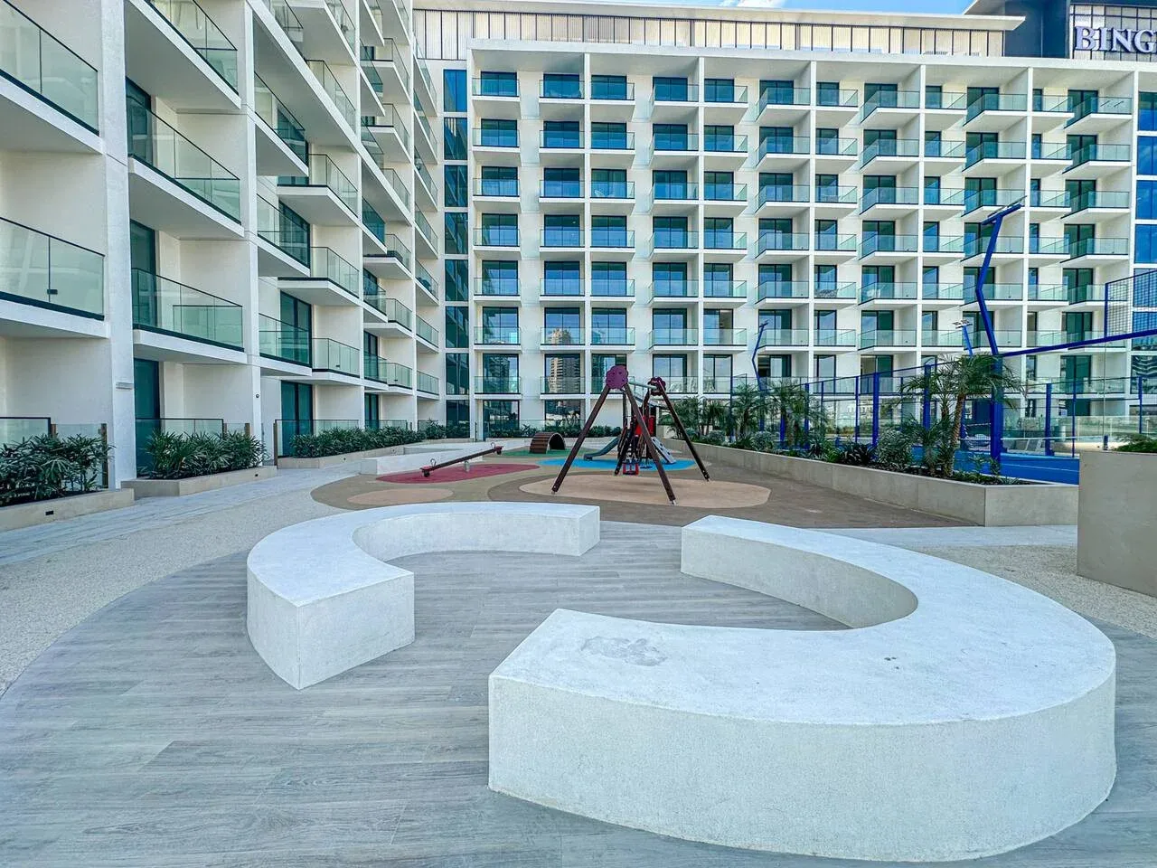 A courtyard playground with a small climbing structure and curved white seating.