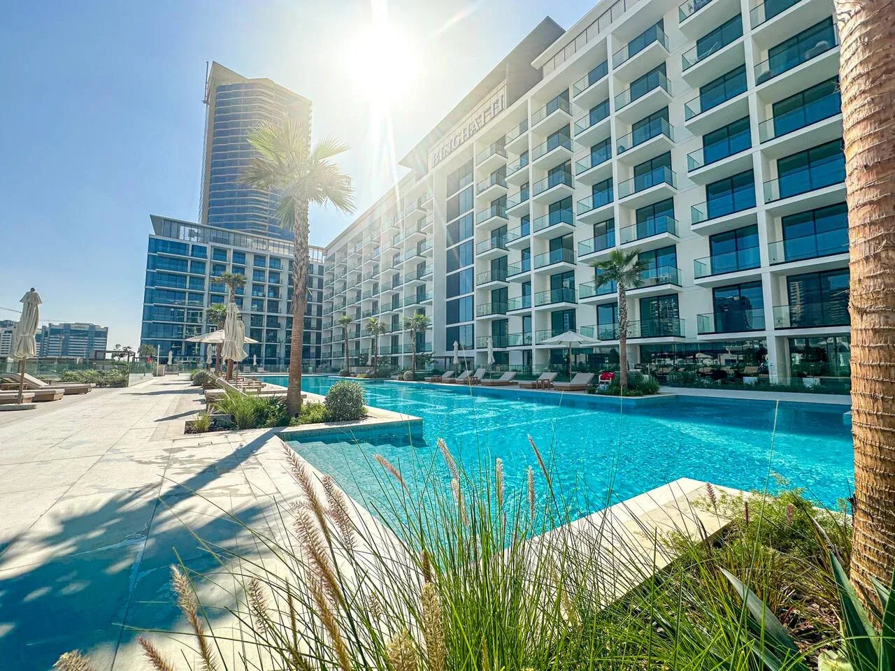 A swimming pool beside a modern multi-story building on a sunny day.
