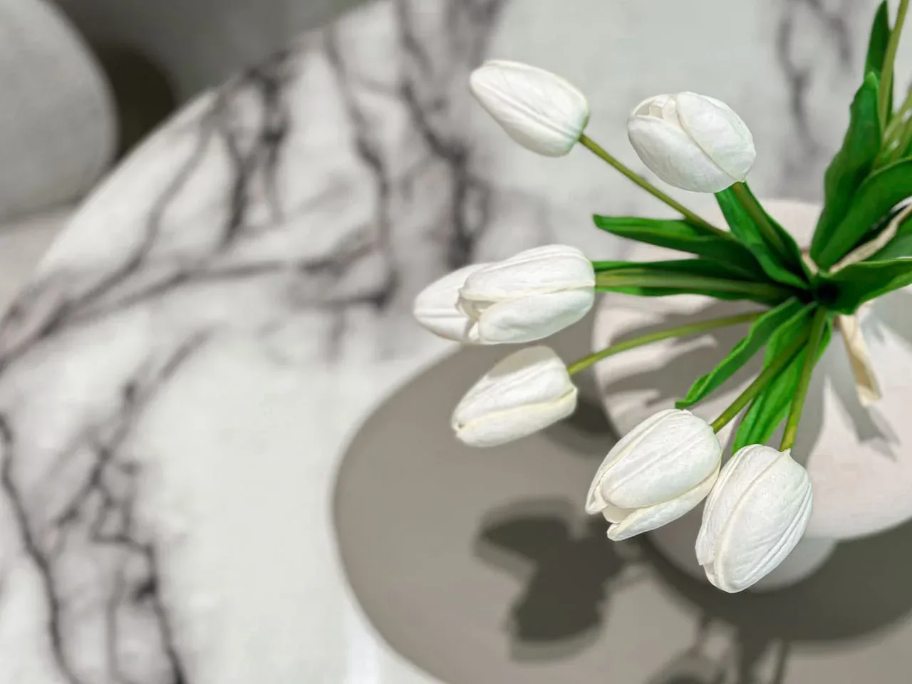 A white flower arrangement rests on a round table with a marble-patterned surface.