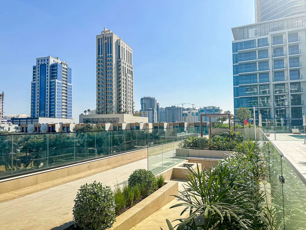 An outdoor terrace with planted beds and glass railings overlooks nearby high-rise buildings.