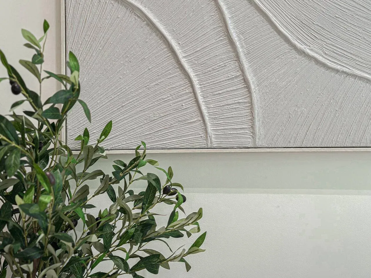 A leafy plant stands beside a large textured abstract wall artwork.