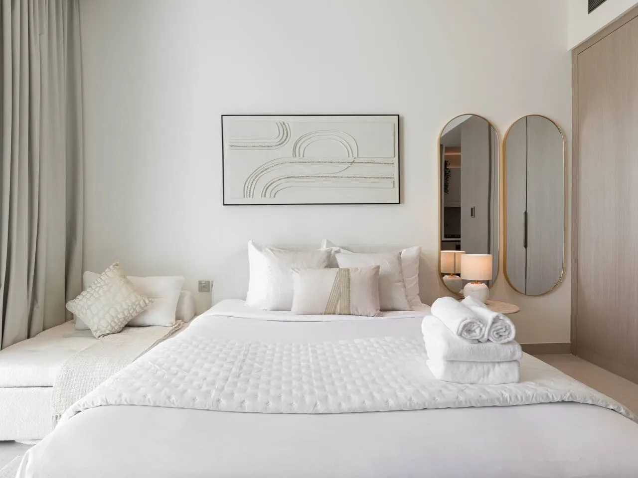 A neatly made bedroom with white bedding and framed abstract artwork above the bed.