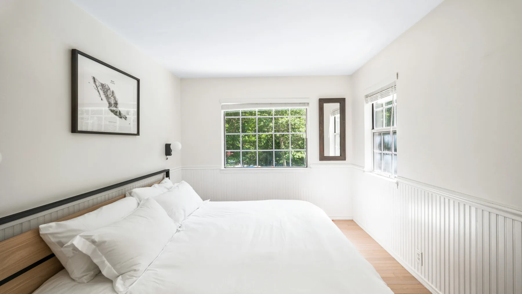 Un dormitorio luminoso con una cama bien tendida y ventanas con vista a zonas verdes.