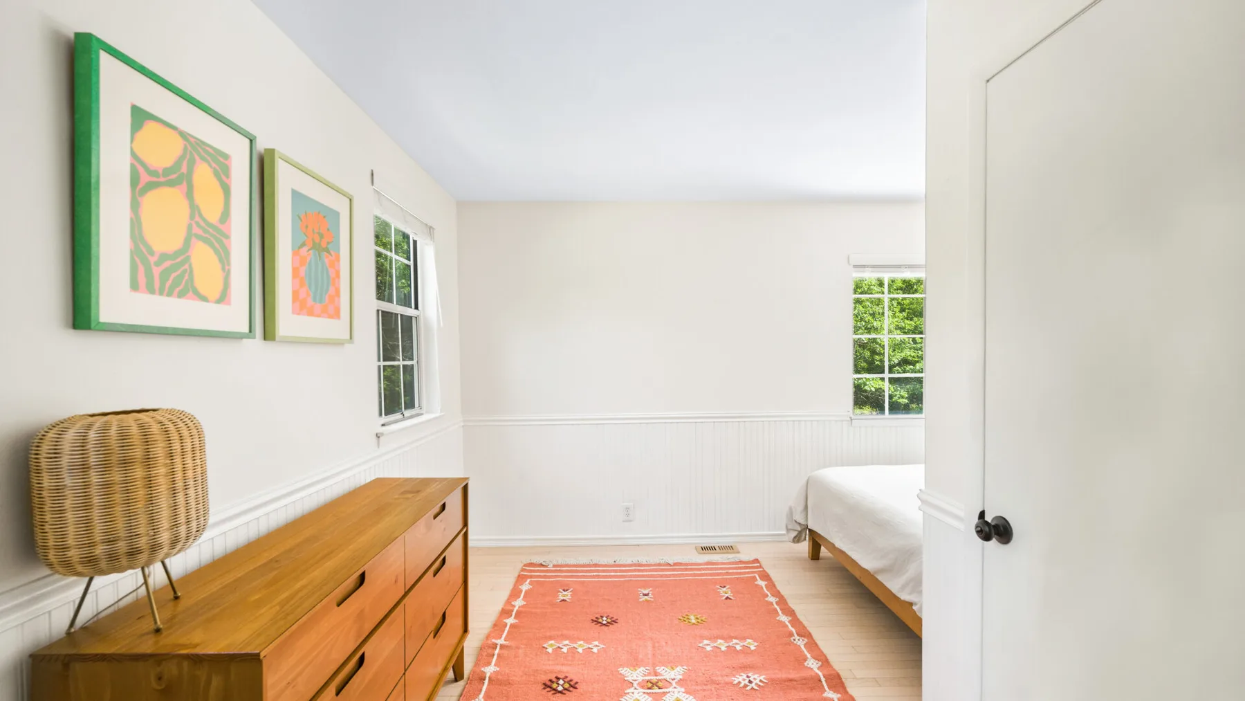 Un dormitorio luminoso con una cómoda de madera y una alfombra estampada.