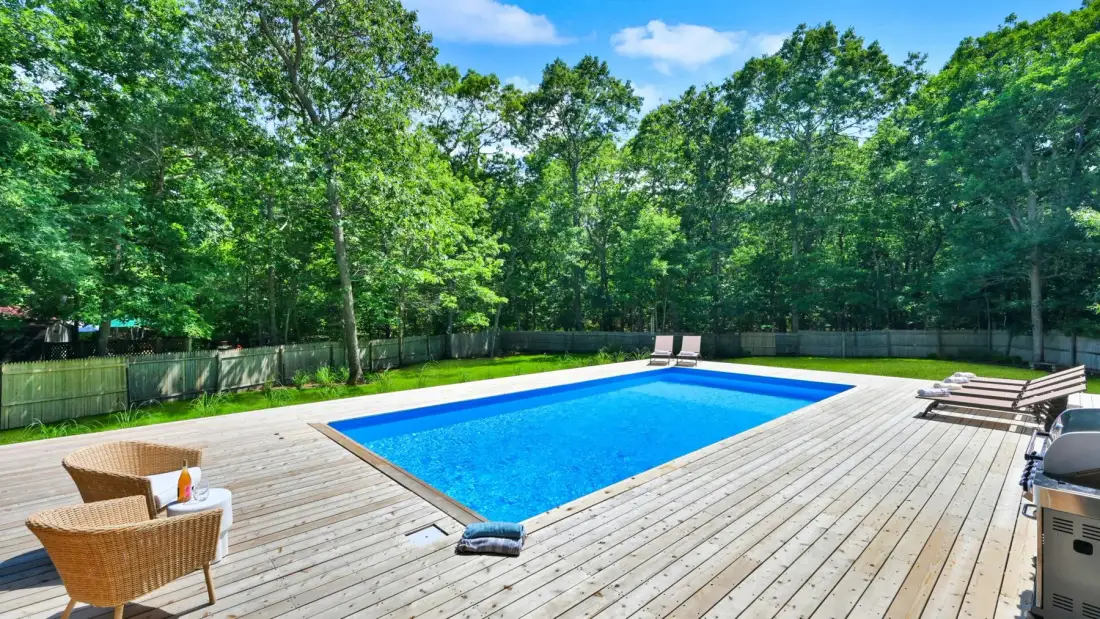 Una piscina al aire libre está rodeada por una amplia terraza de madera y árboles.