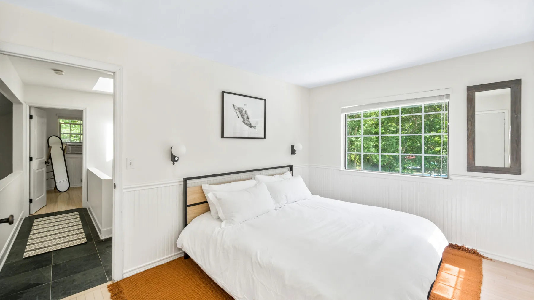 Un dormitorio luminoso con una cama blanca y una ventana grande.
