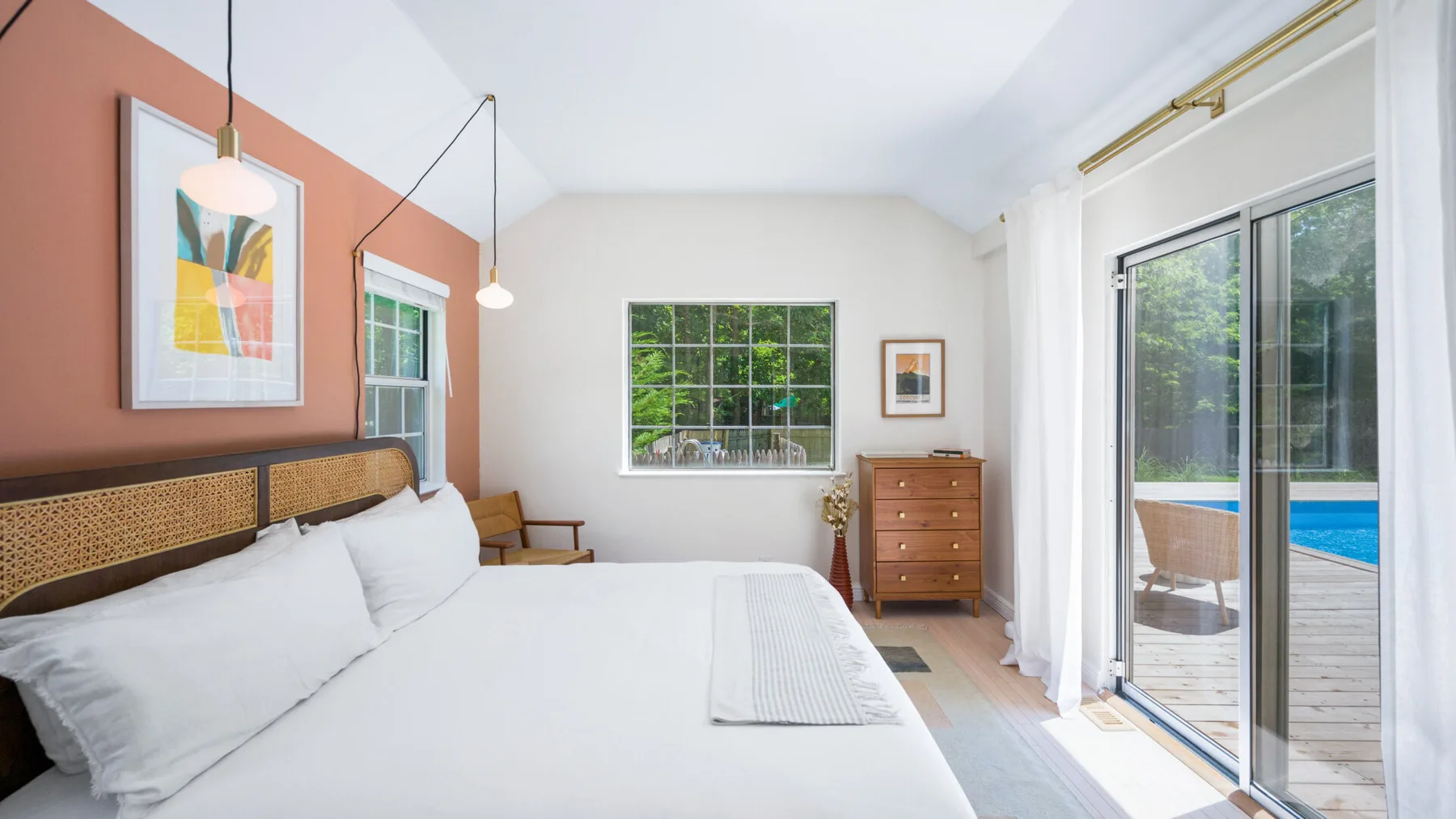 Un dormitorio luminoso con una cama grande y puertas corredizas de vidrio que dan a una terraza junto a la piscina.