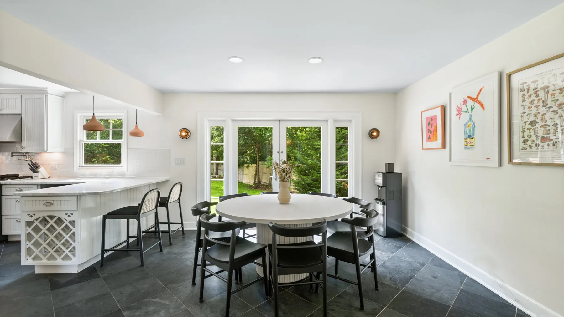 Una luminosa cocina-comedor tiene una mesa redonda y grandes puertas de vidrio con vegetación al otro lado.