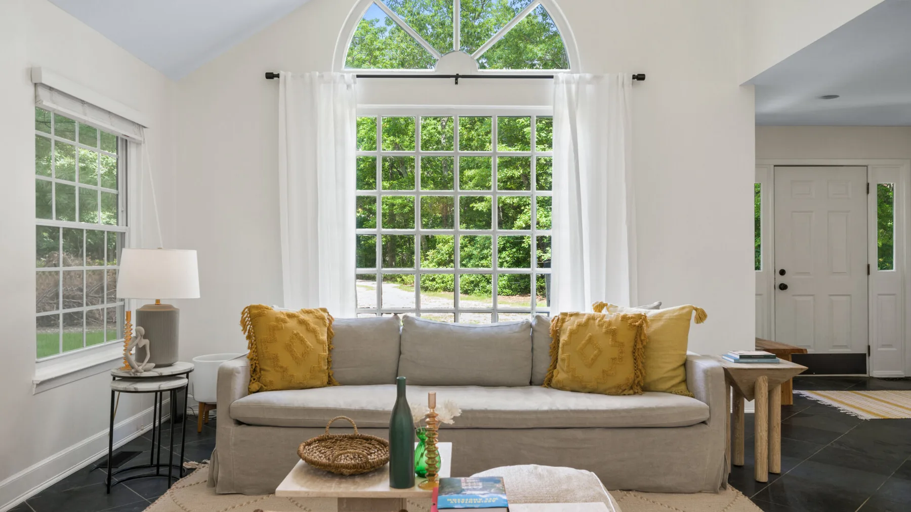Una sala de estar luminosa con un sofá bajo grandes ventanas.