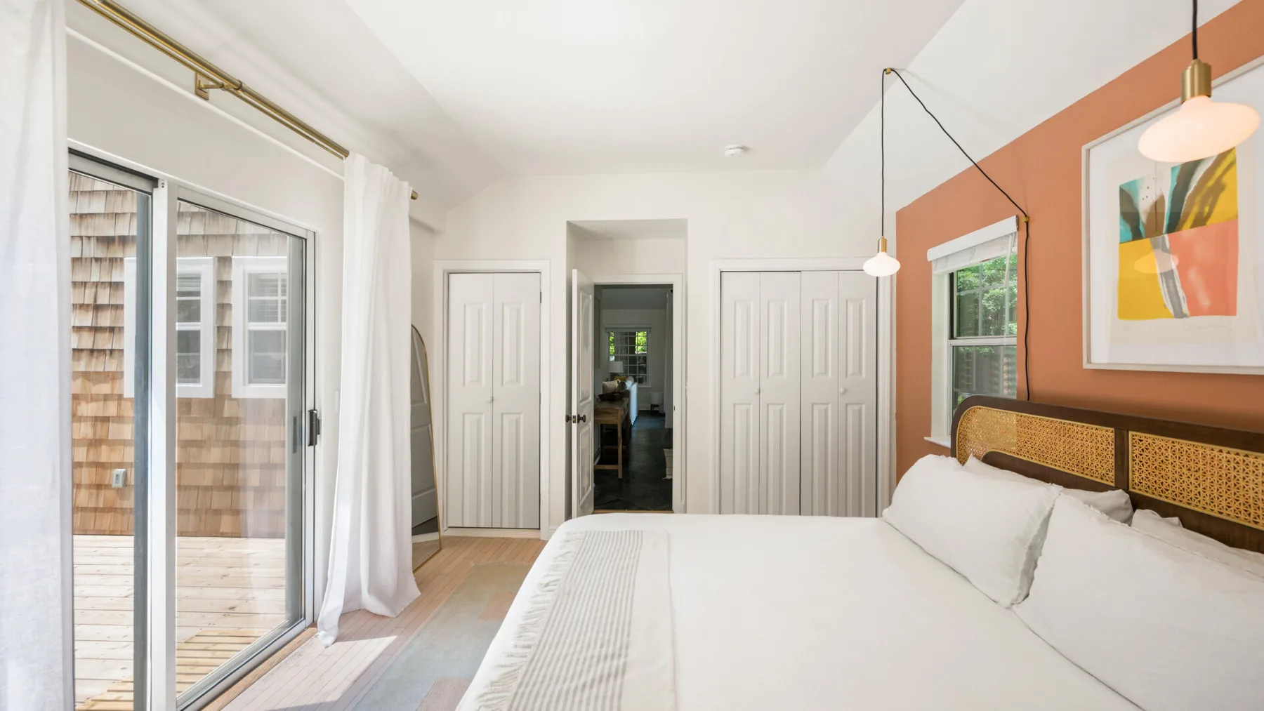 Un dormitorio luminoso con una cama grande junto a puertas corredizas de vidrio y una ventana con cortinas.