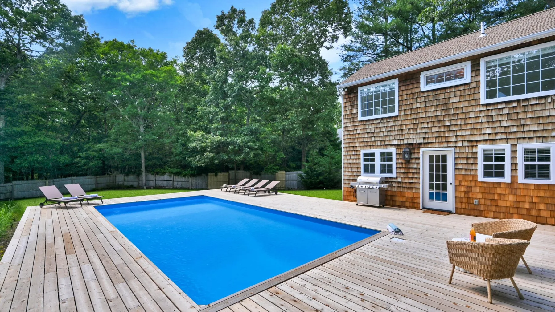 Una piscina en el patio está junto a una casa revestida de madera y una terraza.