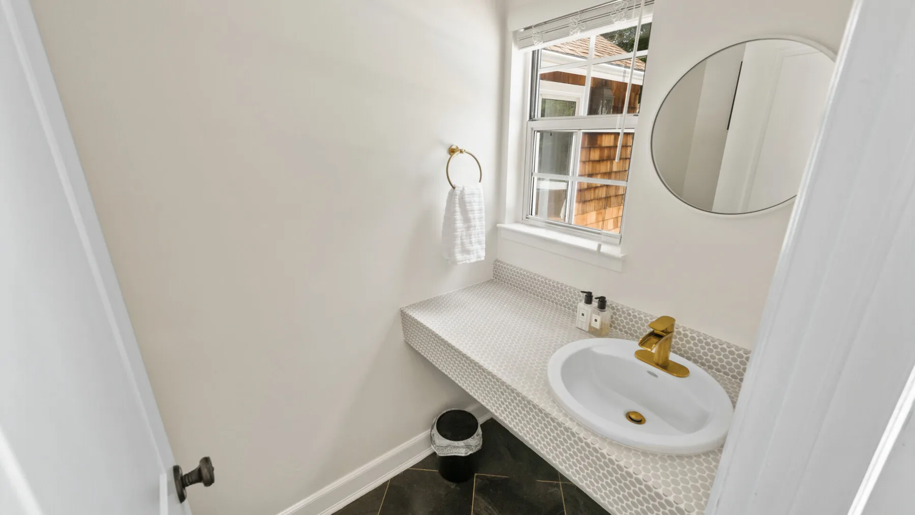 Un baño compacto con lavabo blanco y espejo redondo en la pared.
