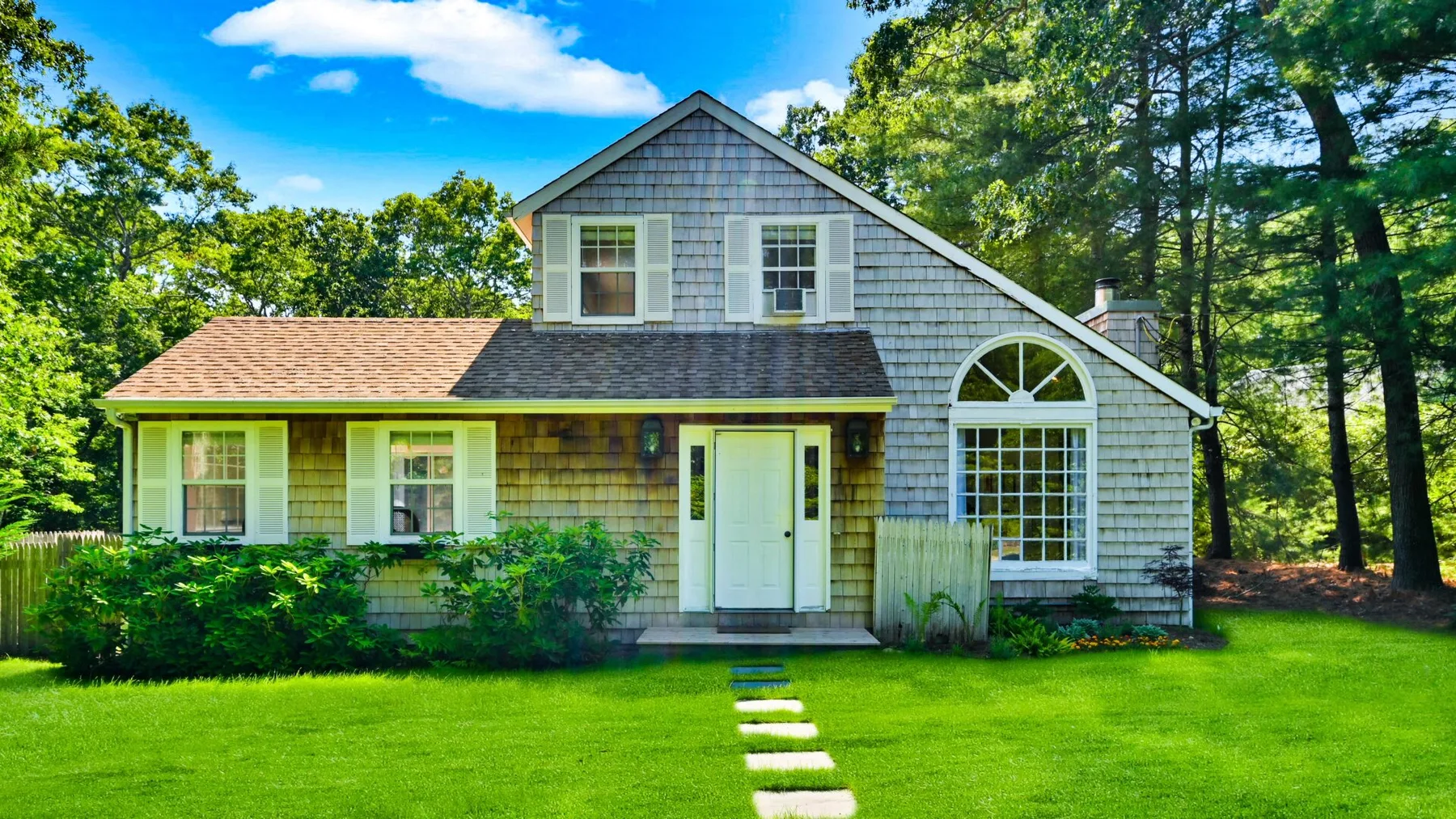 Una casa gris con molduras blancas se alza detrás de un césped verde.