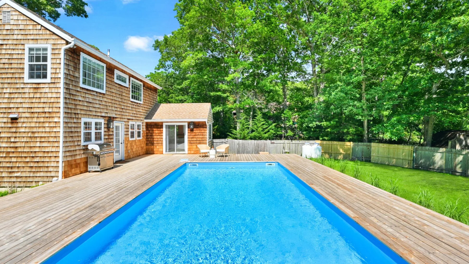 Una piscina al aire libre está junto a una casa de madera y árboles.