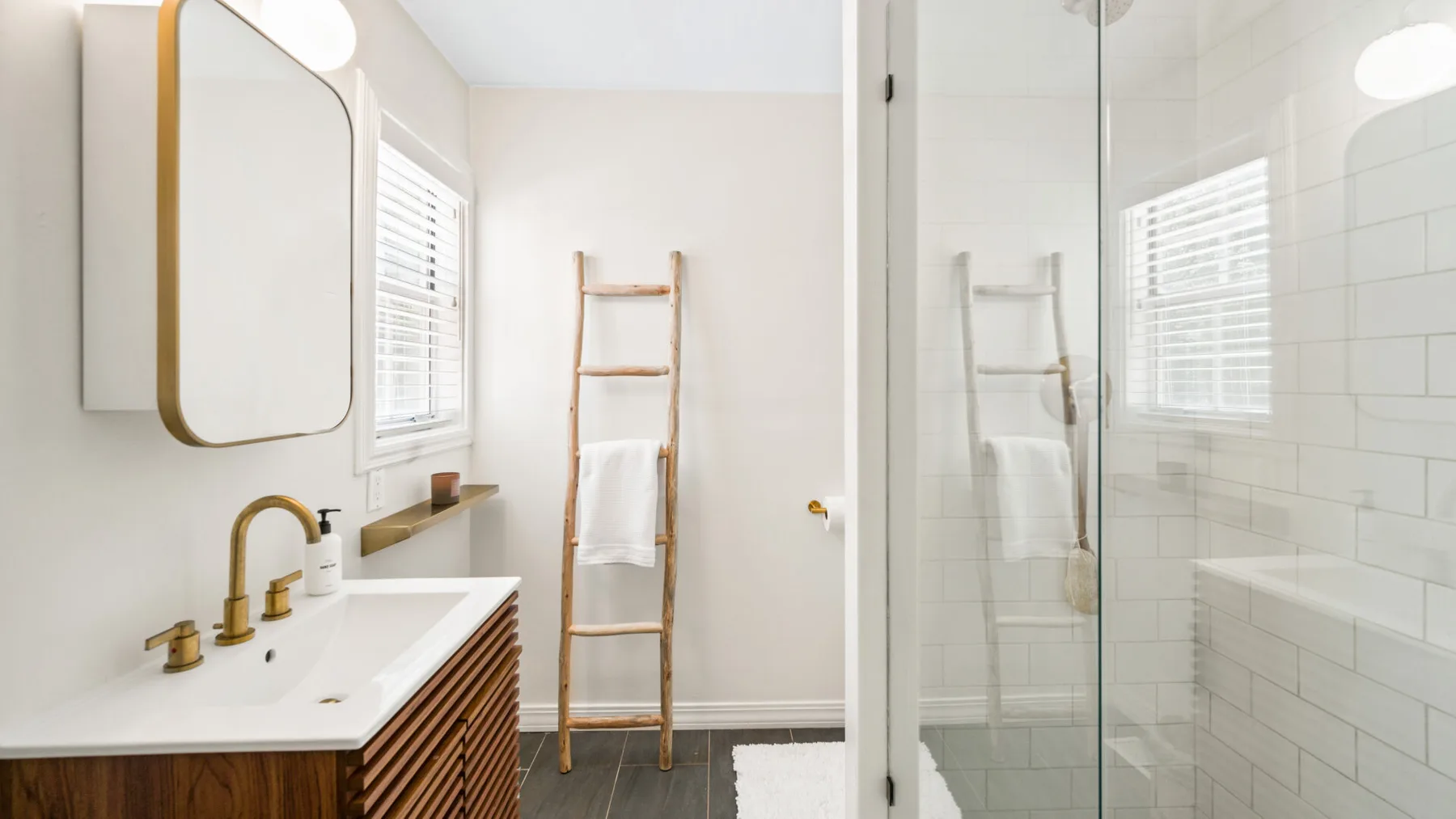 Un baño luminoso con una ducha de vidrio y una escalera de madera para toallas.