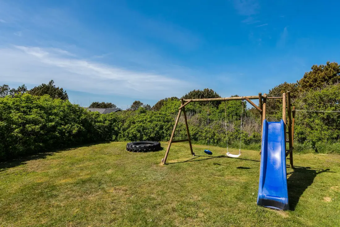 Una zona de juegos al aire libre con césped, columpios y tobogán.