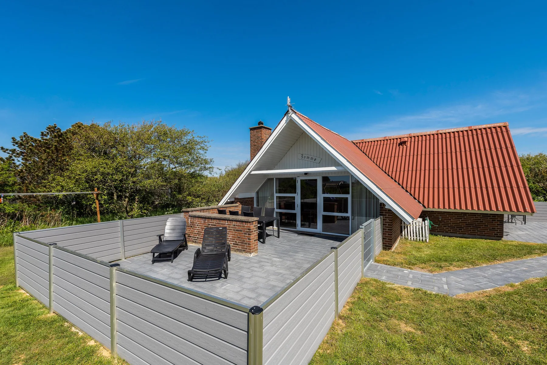 Una casa de vacaciones con patio cercado, asientos al aire libre y techo de tejas rojas.