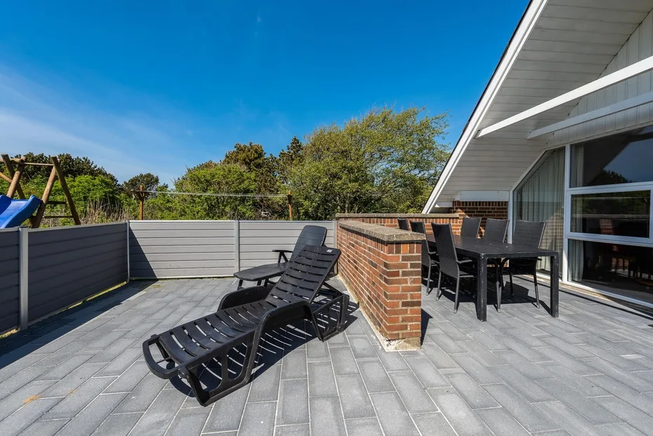 Una terraza exterior pavimentada con asientos reclinables y una mesa de comedor junto a la casa.