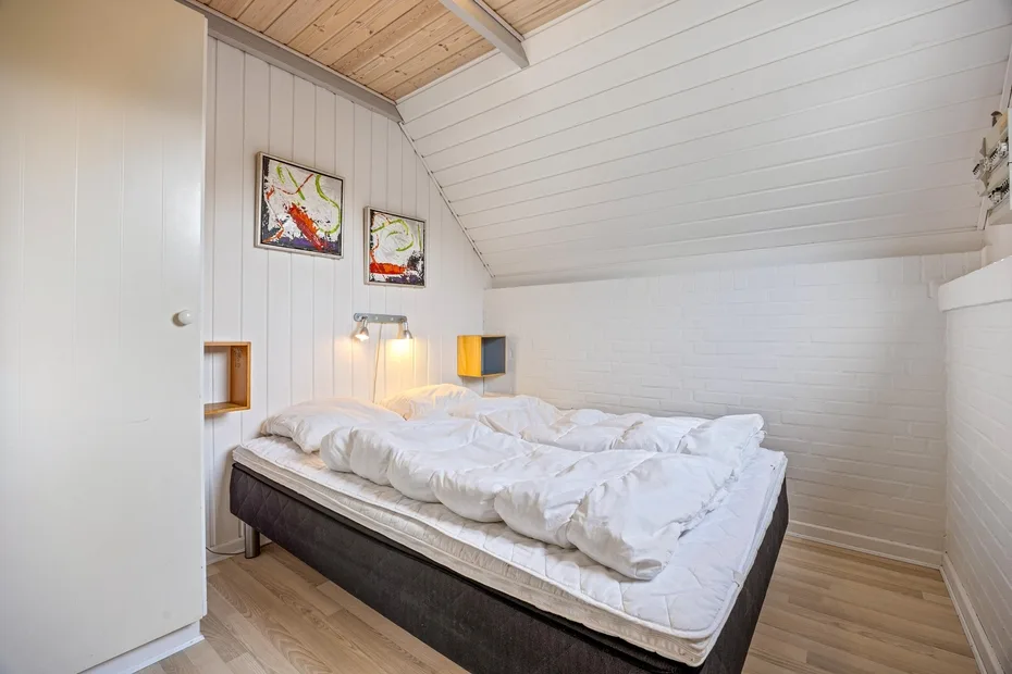 Un dormitorio con una cama bajo un techo blanco inclinado.
