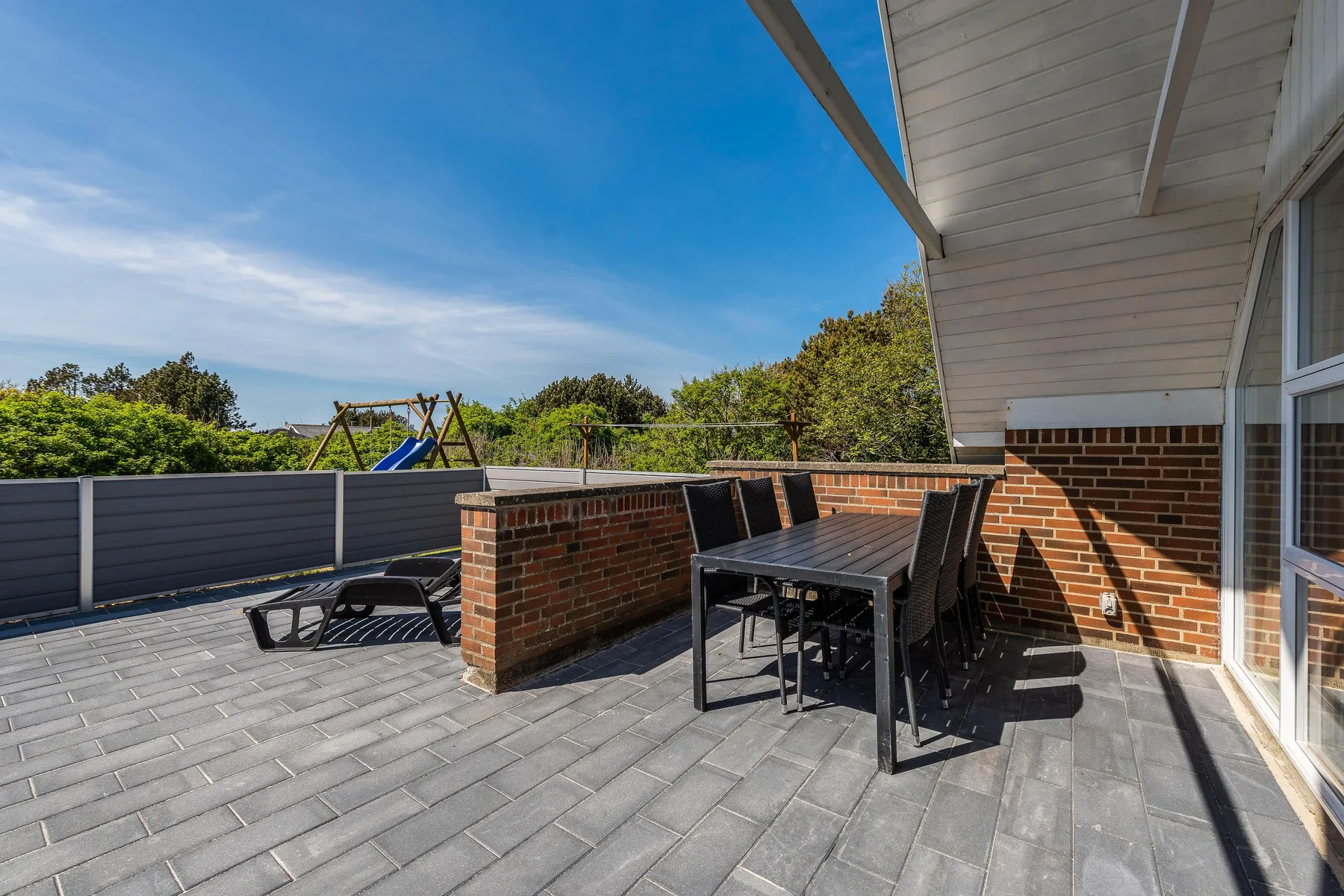 Un patio pavimentado con una mesa de comedor exterior junto a una pared de ladrillo.