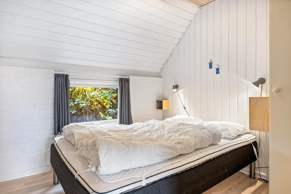 Un dormitorio luminoso con una cama grande bajo un techo blanco inclinado.