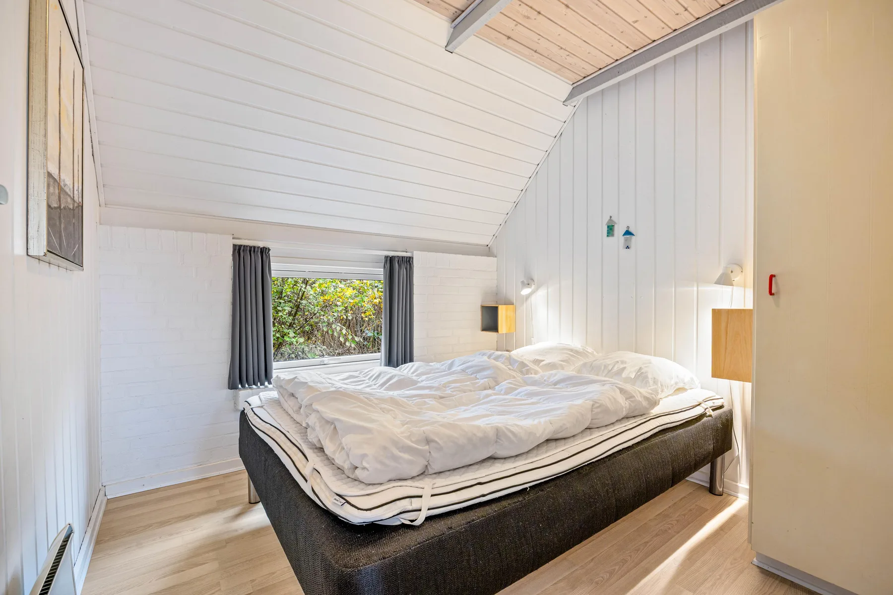 Dormitorio luminoso con una cama grande bajo un techo inclinado.
