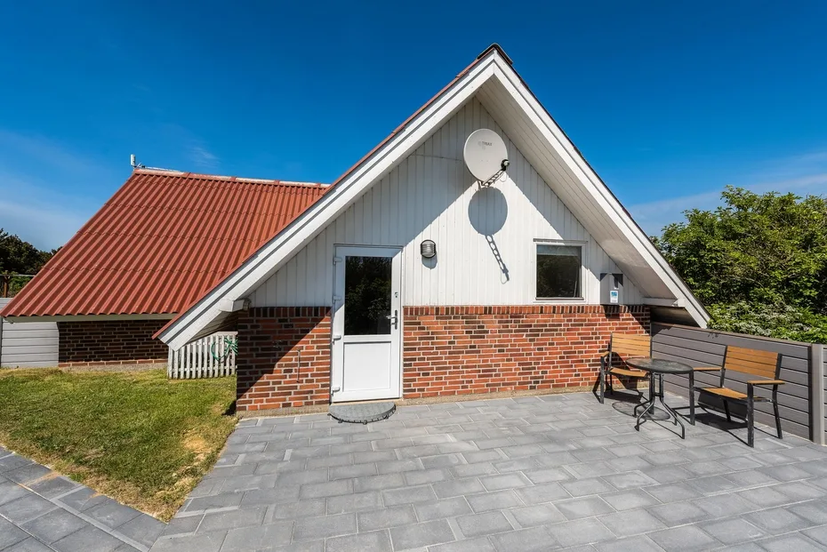 Una casa de ladrillo y blanco tiene un patio pavimentado con asientos al aire libre.