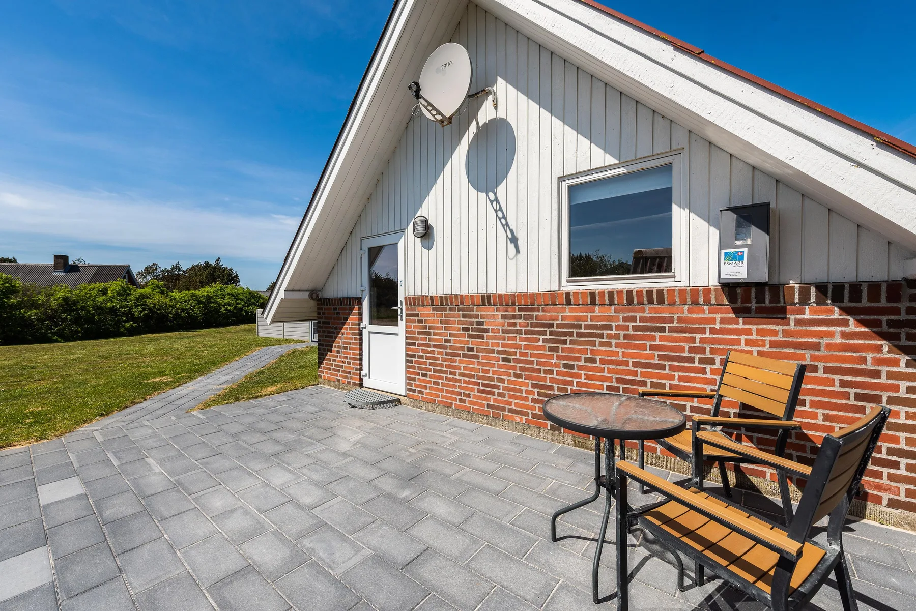 Un patio pavimentado junto a una casa de ladrillo y blanco, con asientos al aire libre.