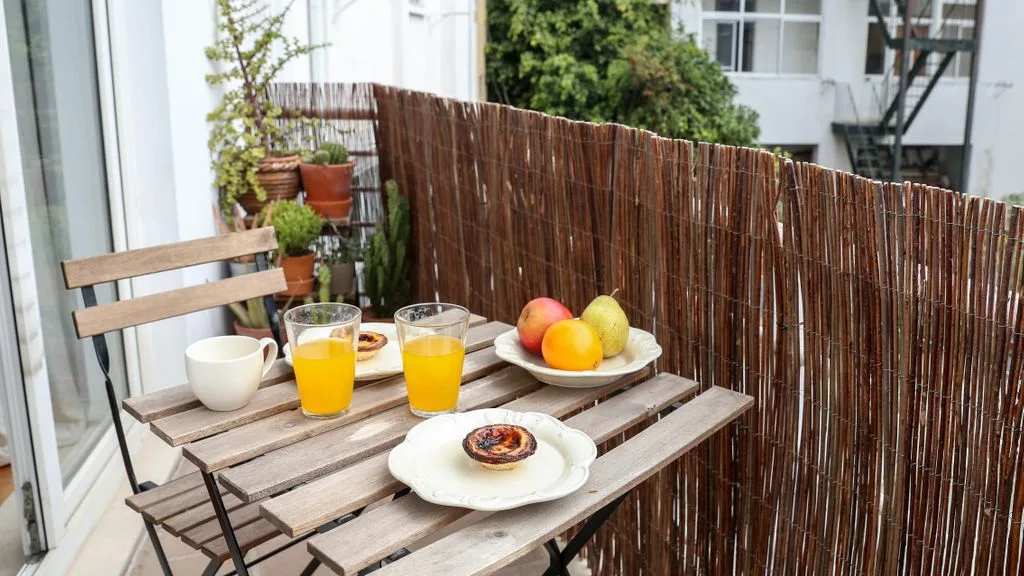 Una pequeña zona de estar al aire libre tiene una mesa de madera con bebidas, fruta y un pastel.