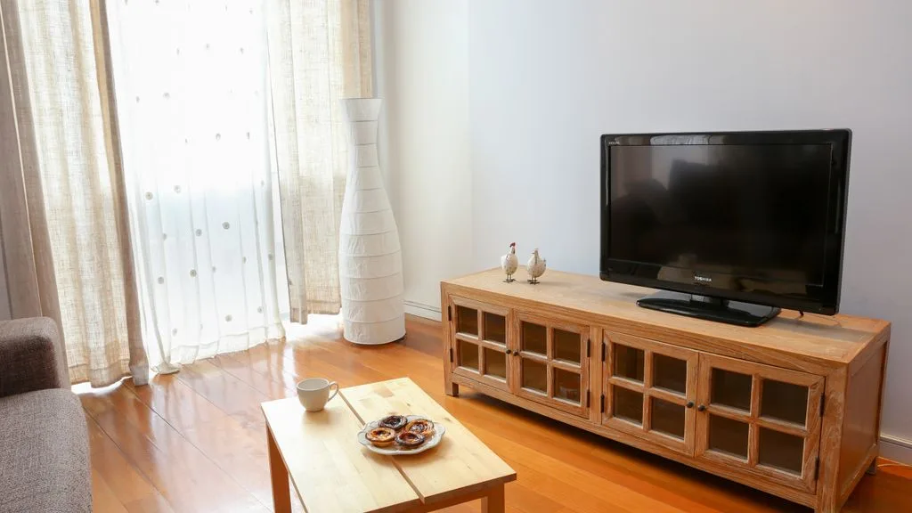 Una sala de estar con un televisor sobre un mueble de madera junto a una ventana luminosa.