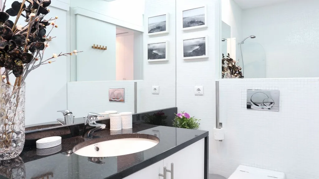 Un baño luminoso con lavabo, encimera oscura y espejo de pared.